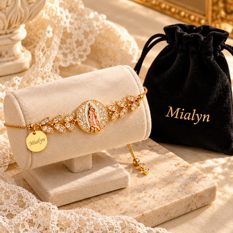 Gold Mother Mary bracelet with engraved name charm on a cream stand beside a black velvet pouch