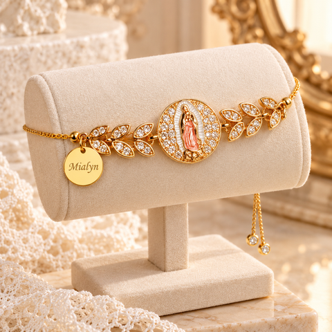 Gold Mother Mary bracelet with leaf links and an engraved name charm on a cream display stand