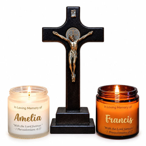 Two lit memorial candles, frosted and amber jars, on either side of a wooden crucifix