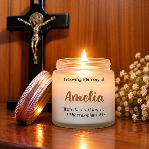 Lit Amelia memorial candle with a rose-gold lid on a wooden table beside a crucifix and white flowers